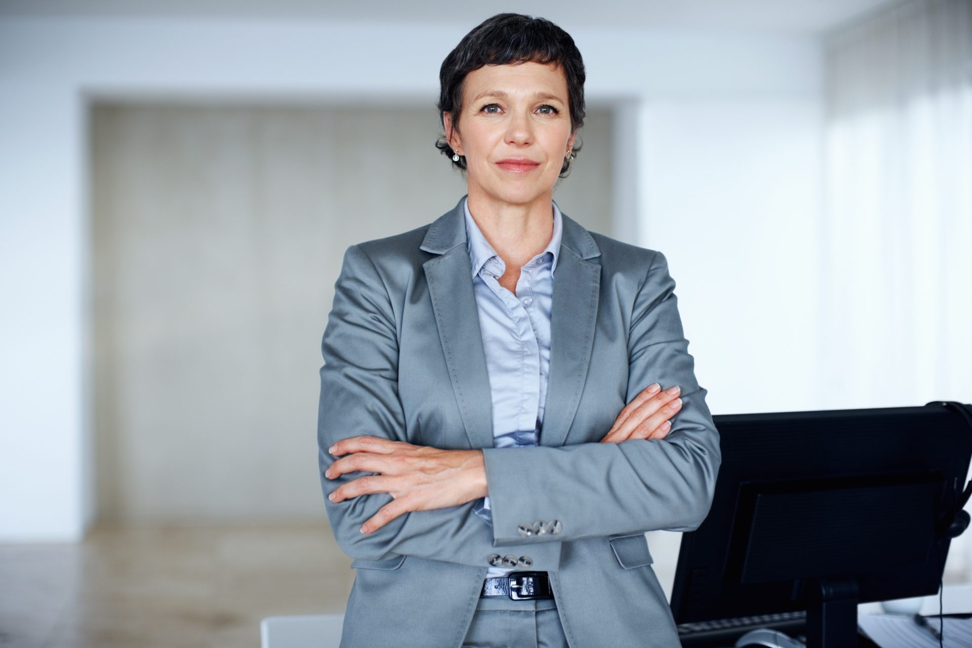 Businesswoman in a gray suit standing confidently with arms crossed, representing leadership and professionalism in a consulting environment.